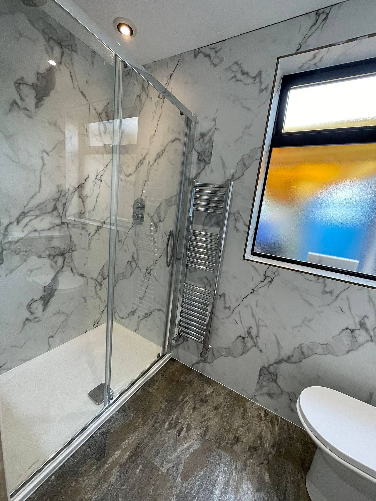 Large shower enclosure with chrome fixtures and a slim width towel radiator in chrome.