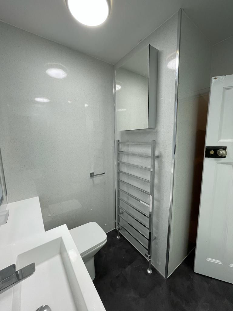 Glossy showerwall throughout entire bathroom, mirrored wall cabinet for additional storage and chrome heated towel rail to compliment the rest of the bathroom.