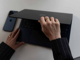 Ruka drží laptop a druhá ho otevírá. Vedle leží mobilní telefon. Obrázek se týká tématu, co je klíčové slovo.