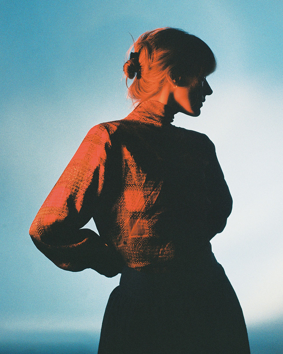 A photograph of a women standing side on with blue and red tones