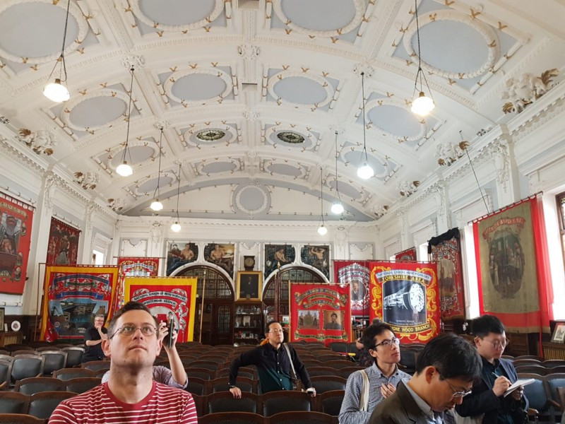 A large hall with banners in the background, in the foreground are people looking at the hall