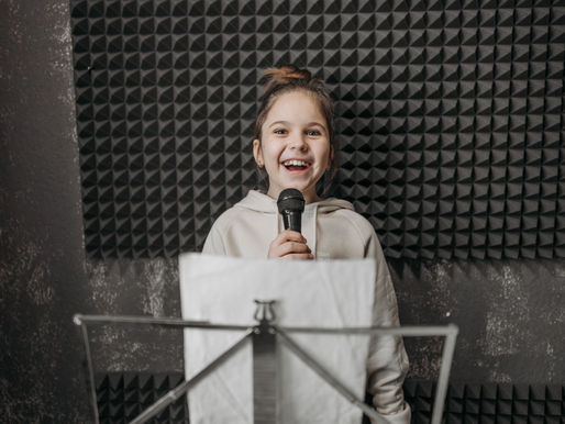 Smiling young girl holding a microphone and happily singing, participating in beginner voice lessons at Kingwood Arts Academy of Music in Kingwood, TX.