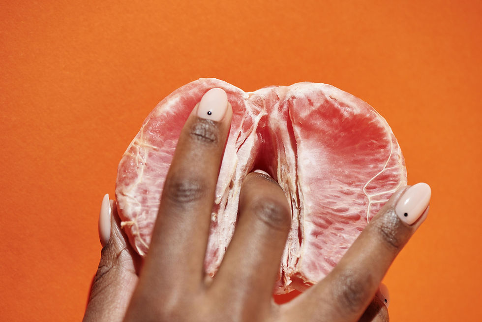A woman's hand playfully interacts with a halved orange, creatively simulating a suggestive gesture against a bold orange background.