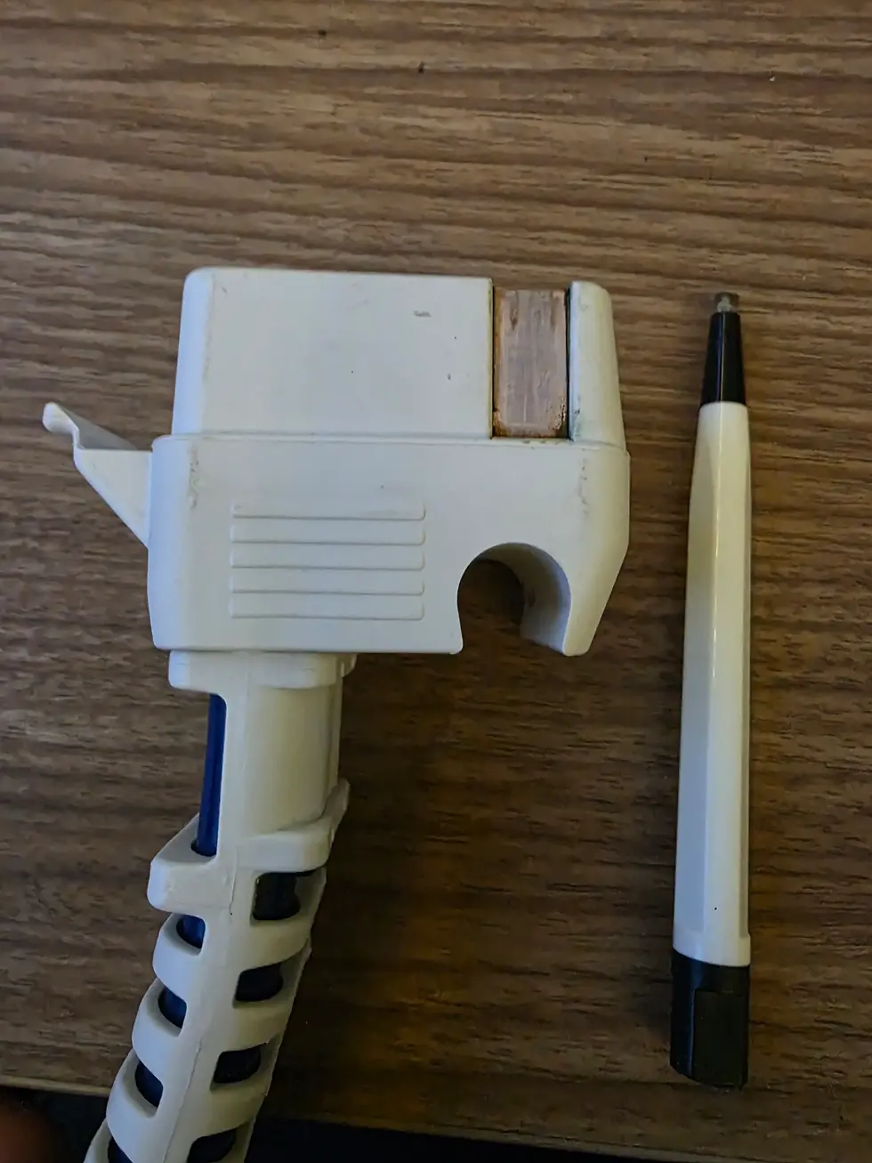 White plastic pump connector and cleaning pen on wooden surface. Clamp has horizontal ridges, pen has a black tip.