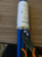 Pliers crimping a hose connector on a blue pipe on a wooden surface. the White Pump has text and a blue arrow pointing downward.