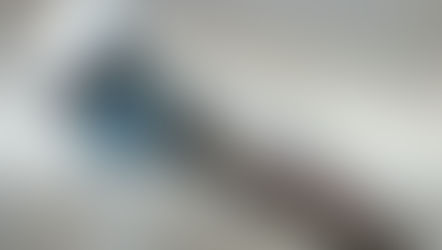 Shiny silver faucet with water pouring out against a blurred beige background. Reflection visible on the metal surface.