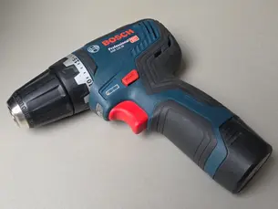 Blue Bosch cordless drill with a red trigger on a light grey surface. Text on drill includes Bosch branding and model info.