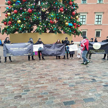Group of 16 diverse Ansar of the Ahmadi Religion of Peace and Light marching at Castle Square in Warsaw, Poland, holding banners and distributing booklets during the December 2025 campaign.
