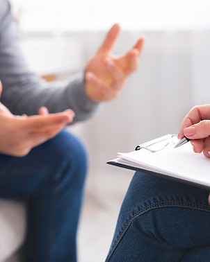 A person is seated in a neutral-colored office space, engaging in a discussion with anothe
