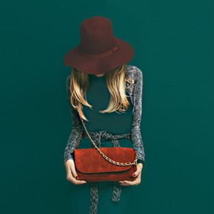 Woman wearing in a matching color dress to the green background. This makes the accessories (hat and purse) pop out and be the focus of the image.