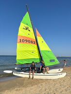 Dwóch mężczyzn na katamaranie z żółto-zielonym żaglem na plaży.