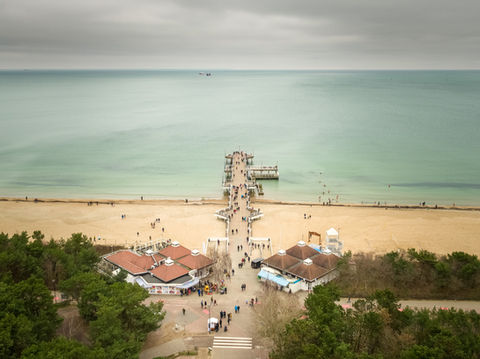 Molo w morzu z piaszczystą plażą, budynkami i ludźmi.