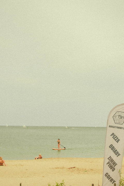 Osoba na desce SUP i inna osoba w wodzie na plaży