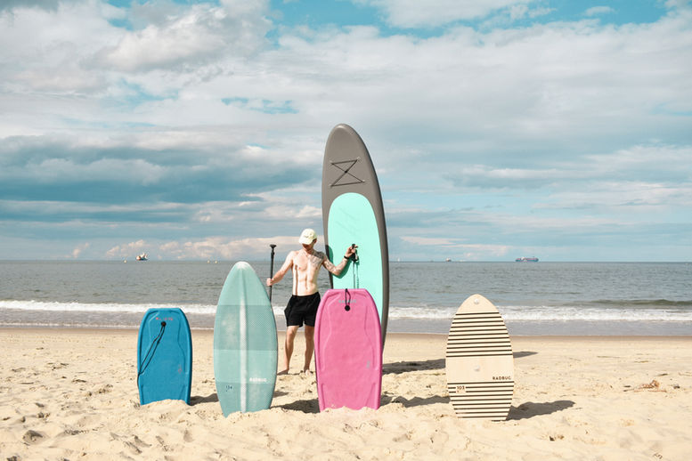 Osoba z wiosłem i deskami surfingowymi na plaży.