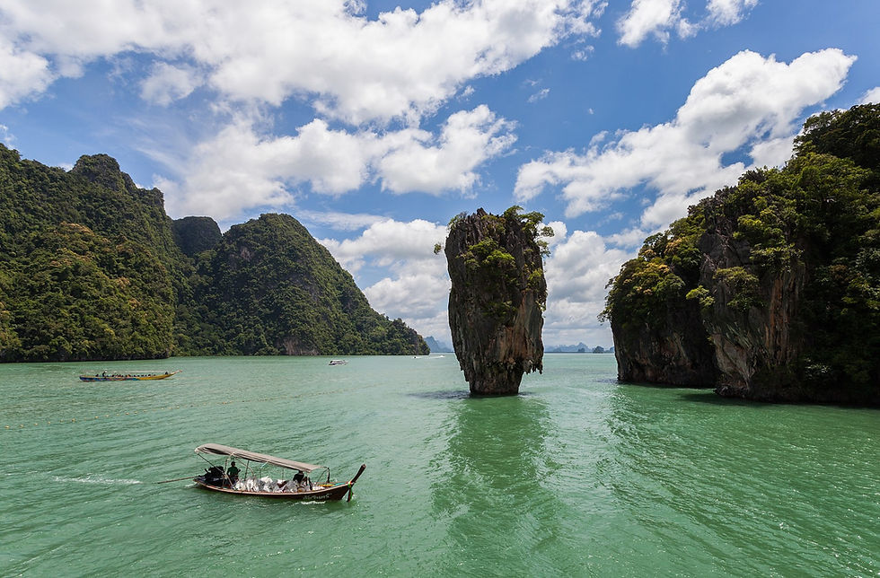 ภาพมุมคลาสสิกของเกาะตาปู (James Bond Island) ในอ่าวพังงา จังหวัดพังงา โขดหินหินปูนสูงกลางทะเลสีเขียวมรกต พร้อมเรือหางยาวลอยอยู่ใกล้ หนึ่งในโลเคชันที่ปรากฏในภาพยนตร์ Jurassic World: Rebirth ในชื่อ “Dinosaur Rock”