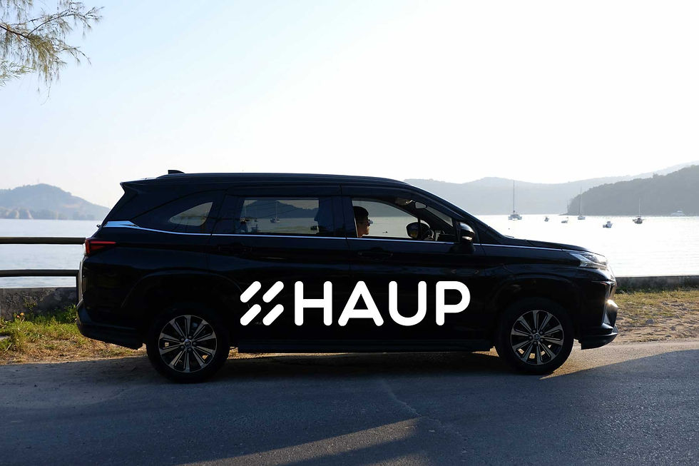 รถ SUV สีดำพร้อมโลโก้ HAUP จอดริมทะเล ท่ามกลางวิวภูเขาและเรือยอชต์