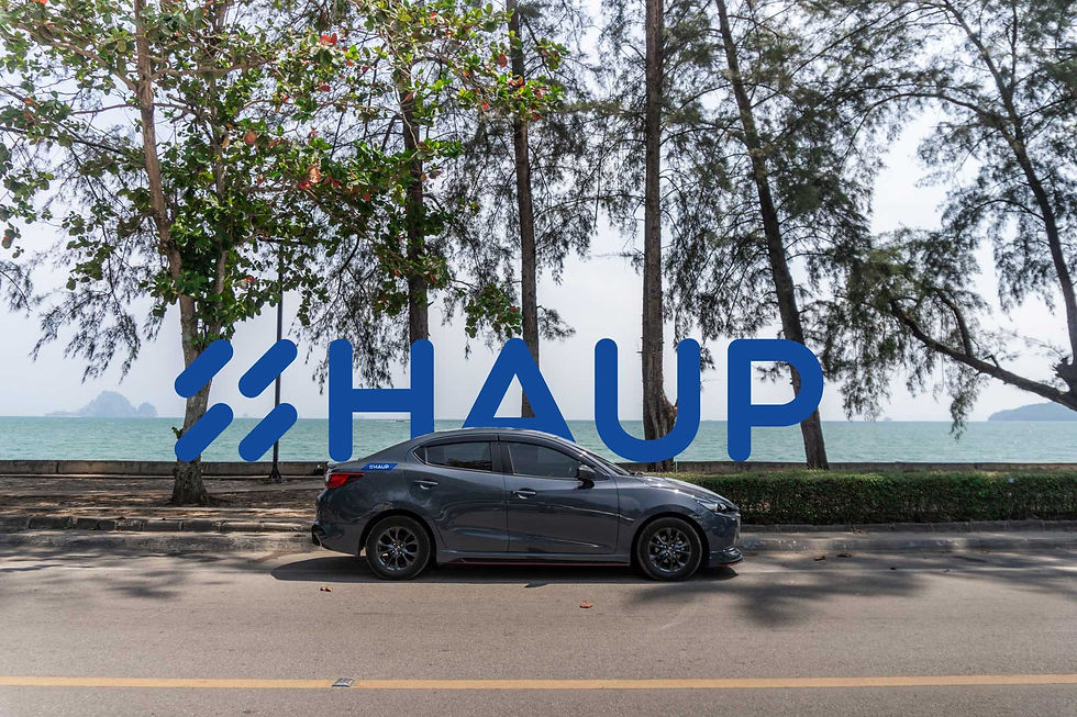 รถเช่า HAUP สีเทาดำจอดอยู่ริมถนนเลียบชายทะเล มีต้นสนทะเลและท้องทะเลเป็นฉากหลัง โปรโมตบริการเช่ารถจากสนามบินทั่วประเทศไทยโดย HAUP