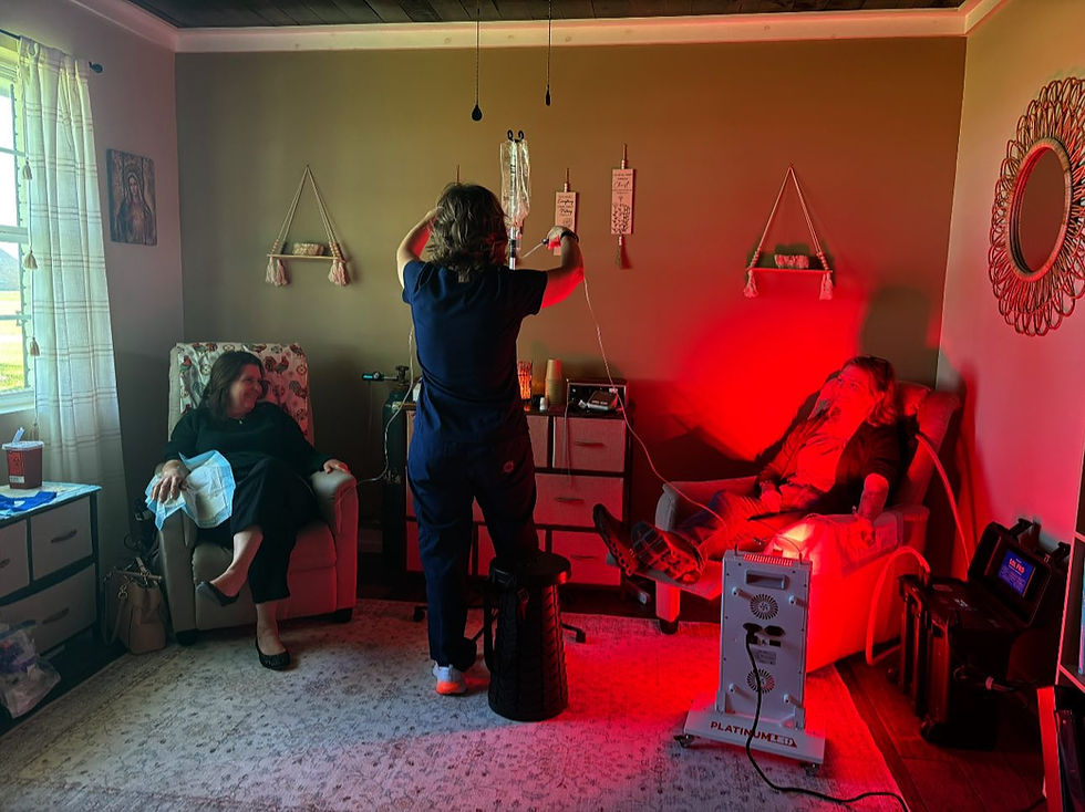 Three people in a warmly lit room; one adjusts IVs while two sit in recliners, one under red light therapy. Cozy decor and patterned rug.