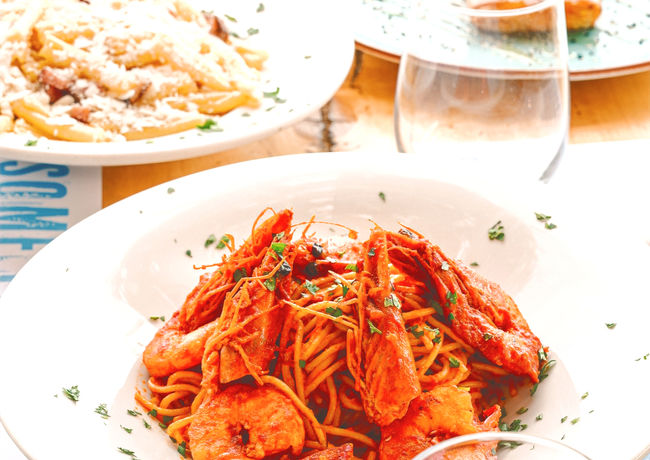 Plates of seafood pasta with large shrimp on a restaurant table.