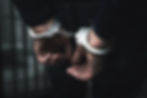 arrested man with cuffed hands behind prison bars.jpg