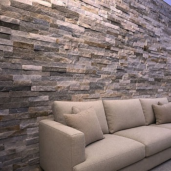 Una pared de piedra de cara dividida en tonos grises y marrones forma un revestimiento rugoso junto a un sofá de color beige.