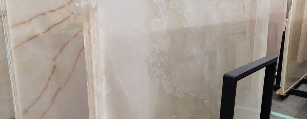 When choosing between natural White Onyx and White Quartz for interior design, understanding their distinct characteristics is crucial. While both offer elegance and versatility, they differ in composition, durability, and maintenance. Onyx consists of large, solid slabs that are meticulously processed to create unique and large panels. Quartz, on the other hand, is more commonly found in smaller sizes in nature. Each stone is individually processed: it is carefully cut, polished, and treated. Then, they are manually assembled into Duramica panels, filled with special compounds, and undergo technological treatments and polishing. Thanks to Duramica technology, quartz can be assembled into large panels, creating durable and striking products. White Onyx: Translucent Luxury with a Delicate Touch White Onyx is a natural stone admired for its translucent beauty and unique veining. Its ability to be backlit makes it a premium choice for feature walls, countertops, and decorative panels.