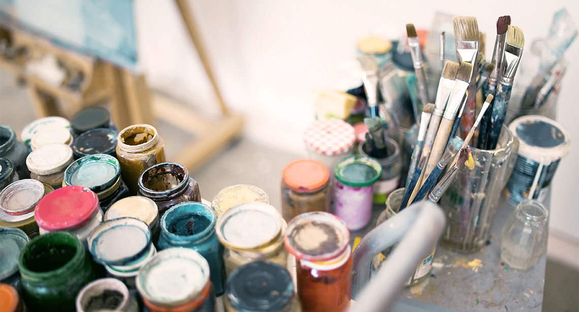 Assorted open jars of paints and brushes