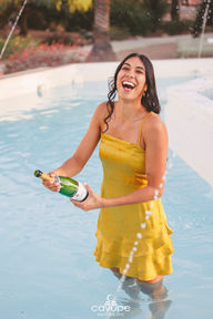 Diana laughing as water splashes around her in the fountain, joyfully holding the champagne bottle.
