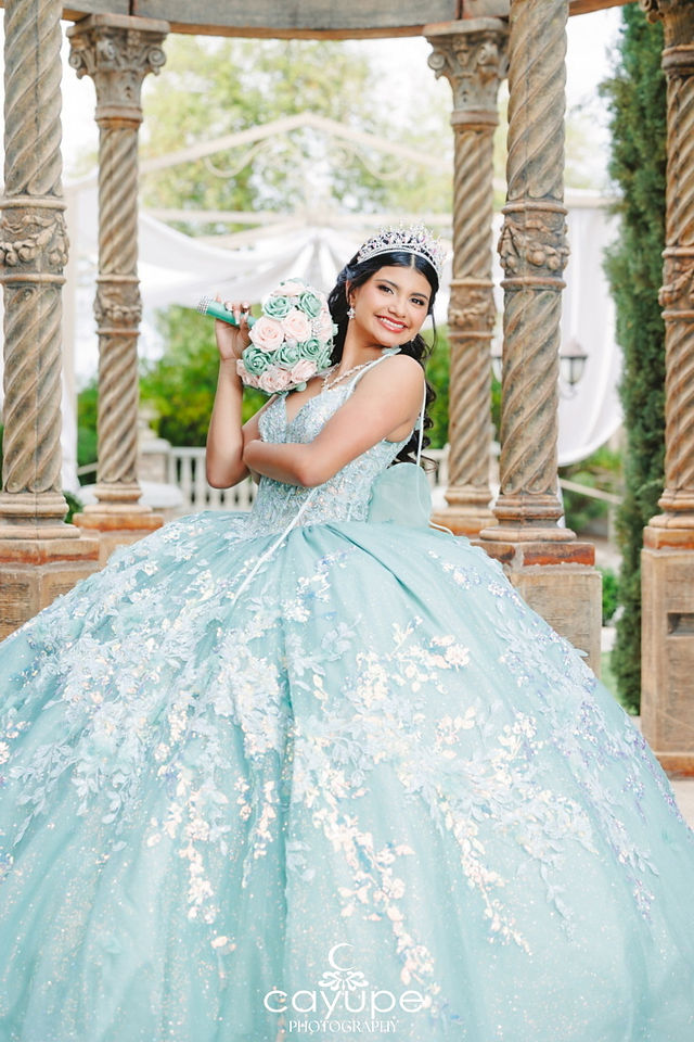 Playful pose of Sabrina resting the bouquet on her shoulder like a baton, turquoise quinceanera gown shimmering under the gazebo’s draped canopy.