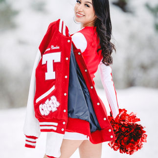 Jasmin looking over her shoulder while holding her cheerleading jacket, with the snow-covered trees in the background