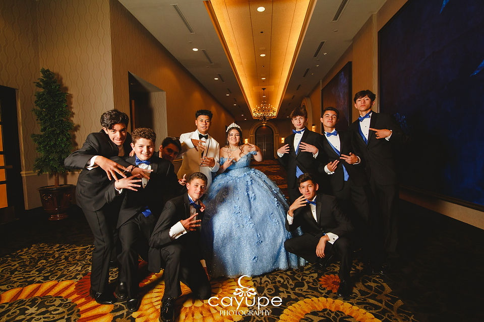 The Quinceanera in her blue gown posing playfully with the male members of her court in tuxedos.