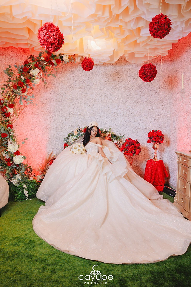 Inside El Mezquite’s reception lounge, Ericka adjusts her tiara on a floral settee, surrounded by red hanging pomanders and roses.