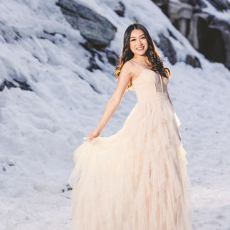 Jasmin twirling in her cream-colored dress, holding the fabric delicately while smiling brightly in a snowy landscape.