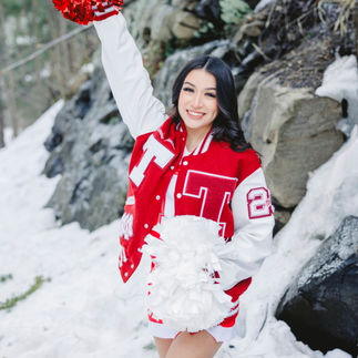Jasmin standing confidently, raising one pom-pom high in the air, with a snowy rock background.