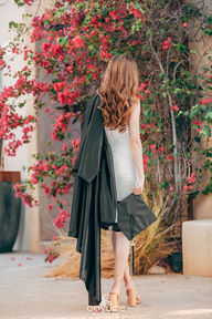 Brenda facing away in a black gown, with pink flowers in the background, radiating elegance.