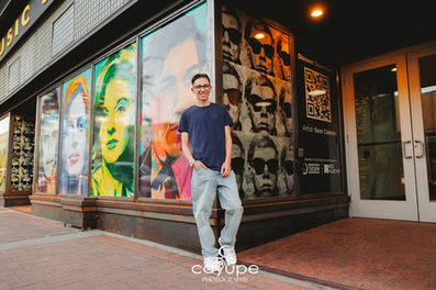 Wide angle senior photo of Israel in front of vibrant mural windows on Congress Street, relaxed stance and easy grin capturing Tucson’s art scene.