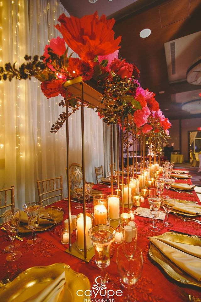 Reception table centerpiece with red flowers, candles, and gold accents, matching the vibrant theme.