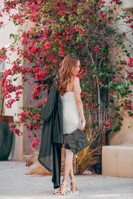 Brenda holding her graduation cap, surrounded by bougainvillea, in a lively environment.