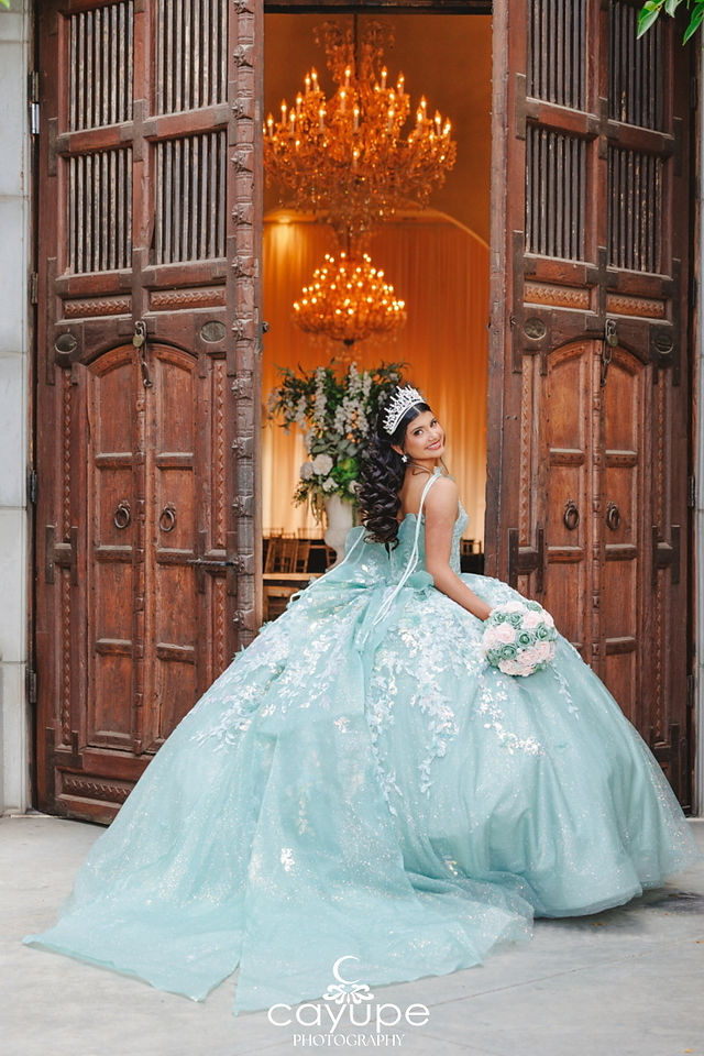 Close up of Sabrina twirling at the castle doorway, her sparkling quinceanera dress fanning out beneath a glowing chandelier inside.