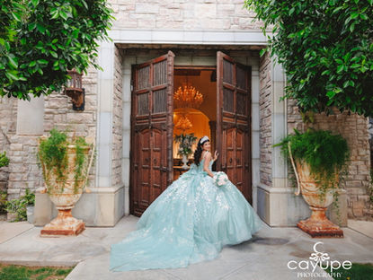 Sabrina steps through the grand wooden doors of Ashley Castle in an aqua ballgown, glancing over her shoulder with a soft smile while greenery frames the entrance.
