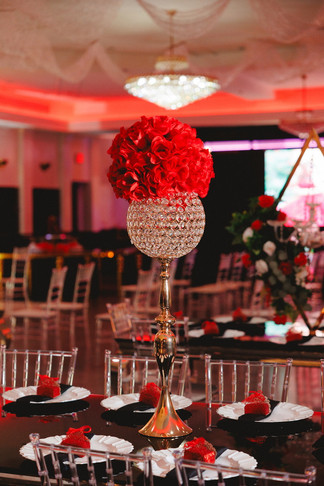Tall crystal vase with red floral arrangement as a centerpiece on a banquet table.