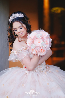 Close-up of quinceanera in a rose gold dress holding a pink bouquet and looking down softly.