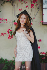Brenda posing elegantly in a patterned white dress and graduation cap, with her hand resting on her hip, showcasing a confident expression.