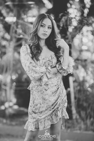 Black and white portrait of Brenda wearing a patterned dress, looking serene, surrounded by nature.