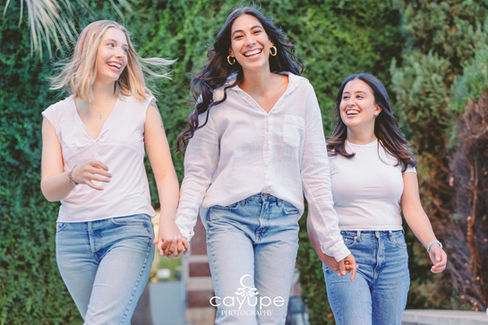 Diana and her friends walk joyfully towards the camera, laughing and radiating happiness in matching white tops and blue jeans, capturing the essence of their friendship.