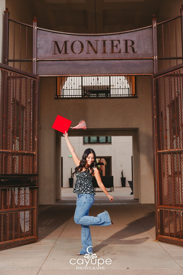 Kristal joyfully posing with her graduation cap under the Monier gate in Tucson.