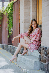 Brenda sitting on stairs, wearing a pink patterned dress and sandals, with a relaxed expression.