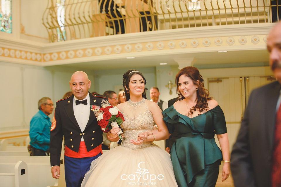 Harlie walking down the aisle at Our Lady’s Chapel, accompanied by her parents, with her father in a Marine uniform.
