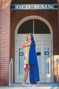 Diana draping her navy blue graduation gown over her shoulder while standing on the steps of Old Main.