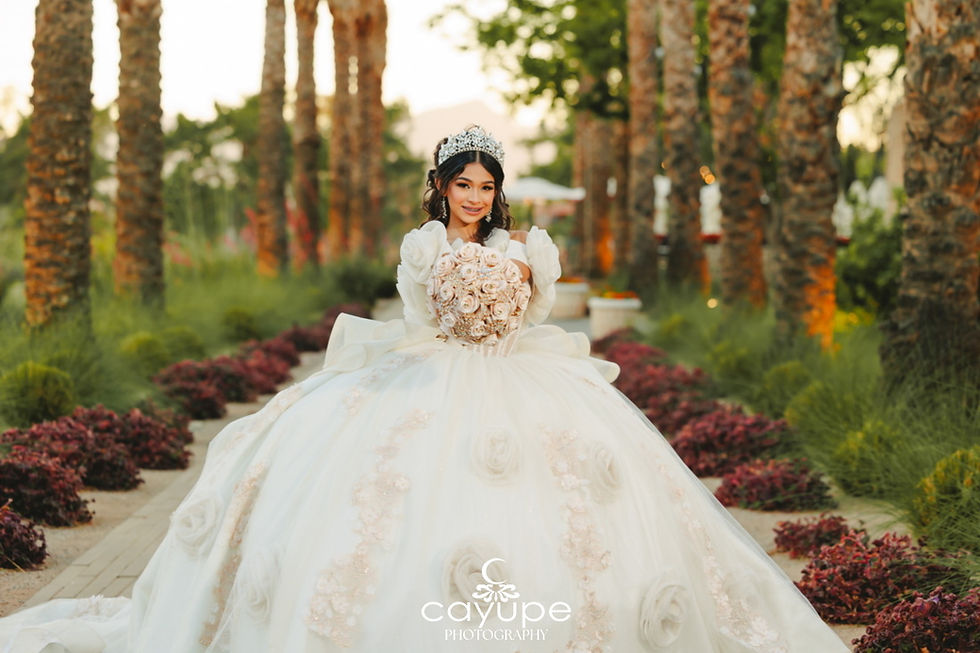 Brianna stands centered on the Avenue of Palms holding a blush bouquet, palm trunks and distant Catalina silhouette framing her quinceanera portrait at Omni Tucson National Resort.